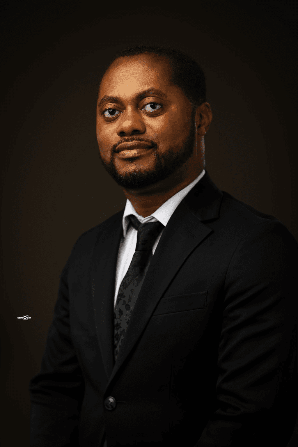 Jonah Kwesi Amponsah in a black suit and tie against a warm dark studio background